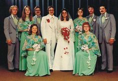 a group of people standing next to each other in front of a metal wall wearing green dresses