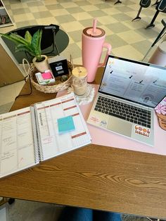 an open laptop computer sitting on top of a wooden desk next to a pink cup