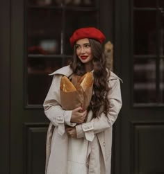 a woman holding a loaf of bread standing in front of a door wearing a red beret