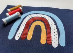 two spools of thread sitting on top of a piece of blue fabric with a rainbow design