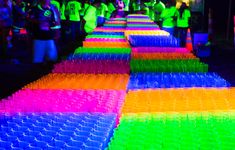 rows of plastic cups are lined up on the floor at a neon party with people standing around