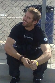 a man sitting on the ground in front of a chain link fence smiling at someone