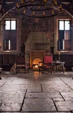 an old fashioned fireplace in the middle of a room with two chairs and a chandelier