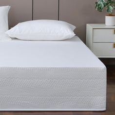 a white bed with two pillows on top of it and a plant in the corner