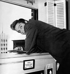 a man leaning on top of an oven in front of a window with shutters