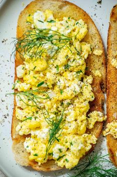 two pieces of bread with scrambled eggs on them and sprigs of dill