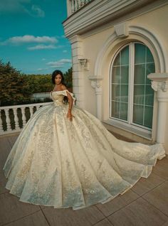 a woman in a white and gold dress standing on a balcony next to a building