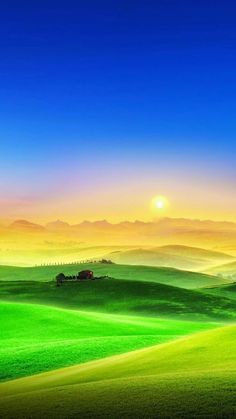 the sun is setting over green hills and fields