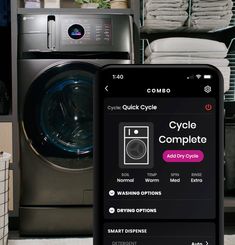 a phone displaying the cycle complete app next to a washer and dryer in a laundry room