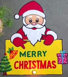 a merry christmas sign with santa claus holding a gift box and lights on the ground