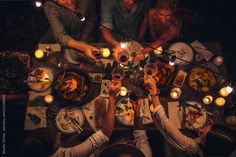 a group of people sitting at a table with food and candles in the dark, overhead view