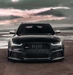 the front end of a black car parked on top of a sandy beach under a cloudy sky