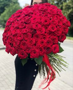 a woman holding a large bouquet of red roses in her hands and wearing black pants