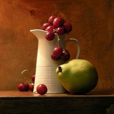 a white pitcher with cherries and a green apple on a table next to it