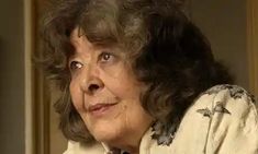 an older woman with curly hair wearing a white shirt and tie looking off to the side