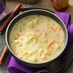 a bowl of soup with carrots, cauliflower and bread sticks on the side