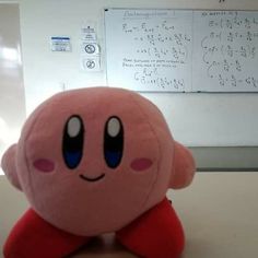 a pink stuffed animal sitting on top of a table next to a whiteboard with writing on it