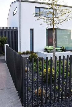 a white house with black iron fence surrounding it and a tree in the foreground