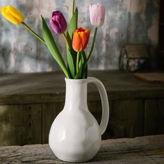 a white vase filled with colorful tulips on top of a wooden table