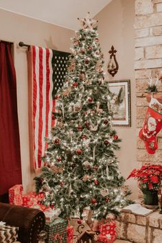 a decorated christmas tree sitting in front of a fireplace with presents on the mantle and an american flag hanging above it