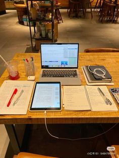 an open laptop computer sitting on top of a wooden desk next to two notebooks