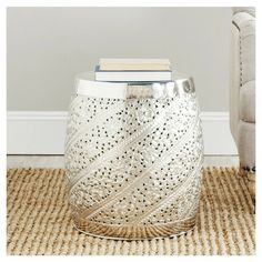 a white vase sitting on top of a rug next to a bookshelf with a book in it