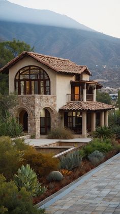 a large house in the middle of some trees and bushes with mountains in the background