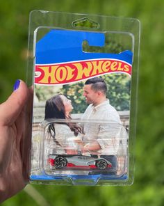 a hand holding a toy car with a man and woman in the back on it