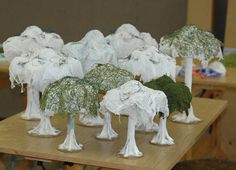 several white trees are sitting on a table with plastic wrap around them and covered in moss