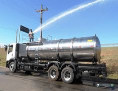 a man sprays water on the back of a tanker truck as it drives down a road