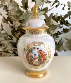 a white and gold urn sitting on top of a table next to a potted plant