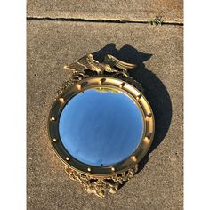 a round mirror sitting on the ground with an eagle decoration around it's edge