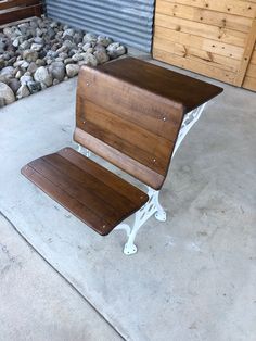 a wooden bench sitting on top of a cement floor next to a pile of rocks