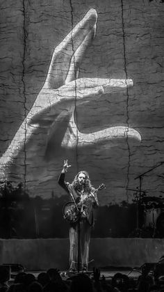 a man standing on top of a stage next to a giant hand holding a guitar