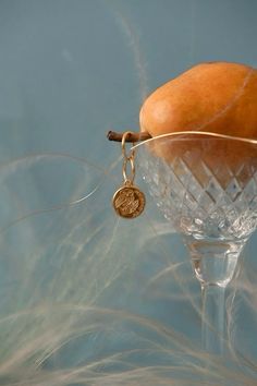 an apple sitting on top of a wine glass with a gold charm hanging from it