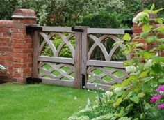 a wooden gate surrounded by lush green grass and flowers in front of a brick wall