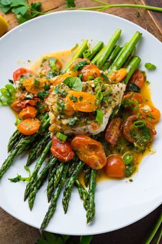 a white plate topped with asparagus, tomatoes and chicken covered in gravy