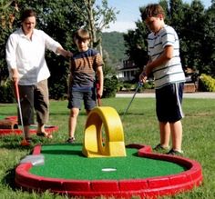 three adults and two children playing mini golf in the grass on a nice sunny day