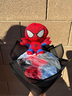 a spiderman stuffed animal sitting on top of a piece of black paper with red, white and blue yarn