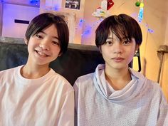 two young men sitting next to each other in front of a tv screen with christmas lights on the wall behind them