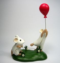 two figurines one is holding a balloon and the other has a mouse on it