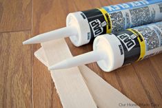 two tubes of glue sitting next to each other on a wooden floor with wood strips