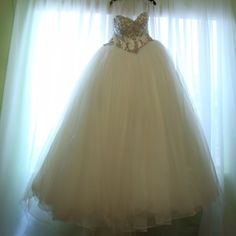 a wedding dress hanging on a hanger in front of a window with sheer curtains