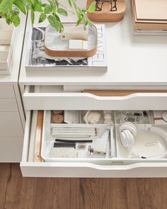 an open drawer in a white desk with books and other office supplies on the table