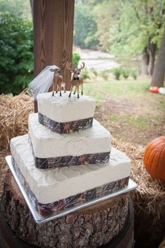 a three tiered wedding cake with deer figurines on top, sitting on a tree stump