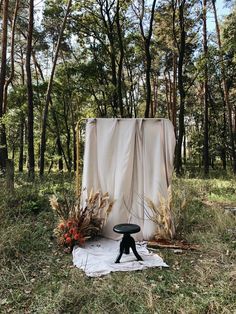 a chair sitting on top of a white sheet in the middle of a field next to trees