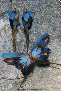 three blue and brown feathers with chains attached to them on a stone surface next to grass