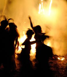 people dancing in front of a fire with their hands up and arms out to the side