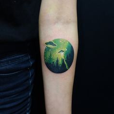 a person with a tattoo on their arm has an alien scene in the middle of it