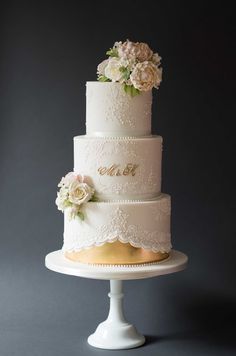 a three tiered wedding cake with white flowers on top and gold trimmings